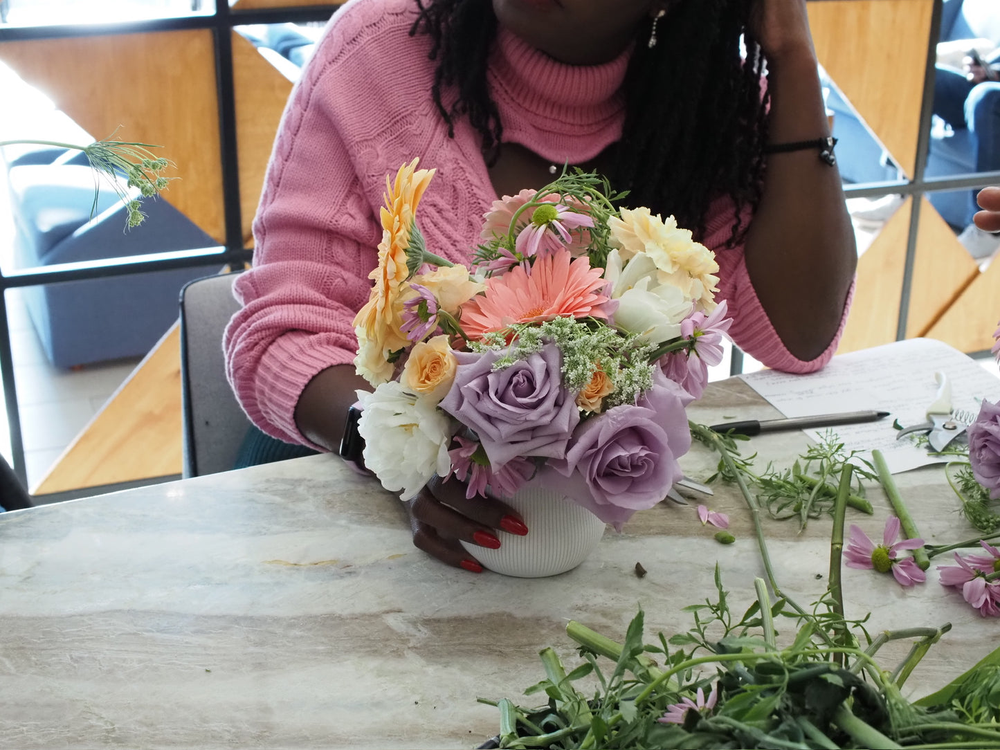 woman holding flower arrangement in white vase containing lavender roses, white tulips, and pink and orange daisies.