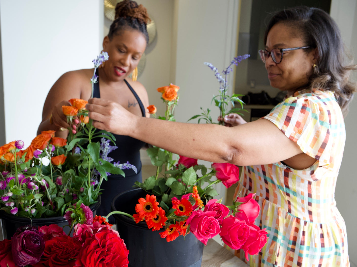 Two women arranging flowers in a room with a neutral background