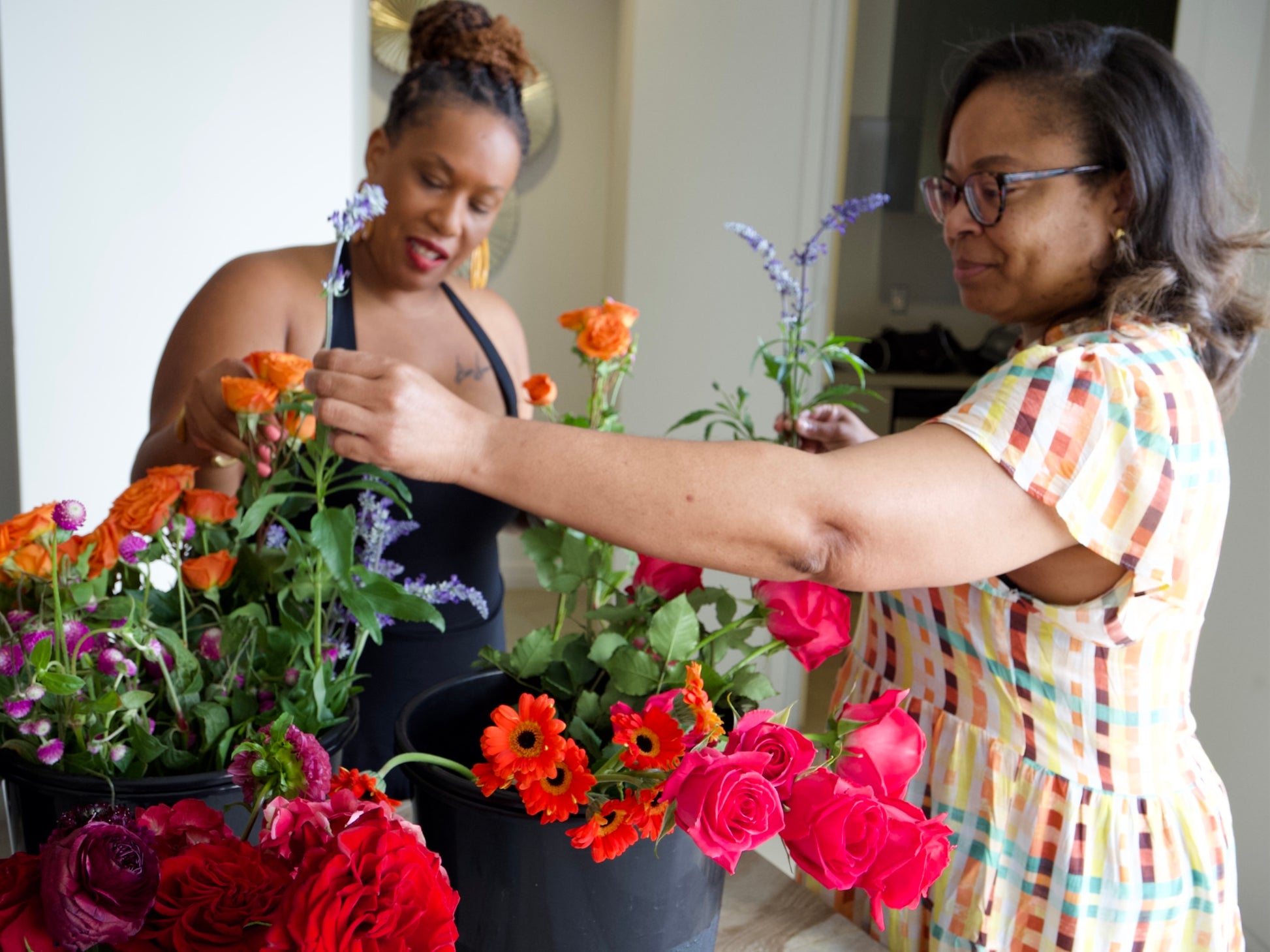 Two women arranging flowers in a room with a neutral background