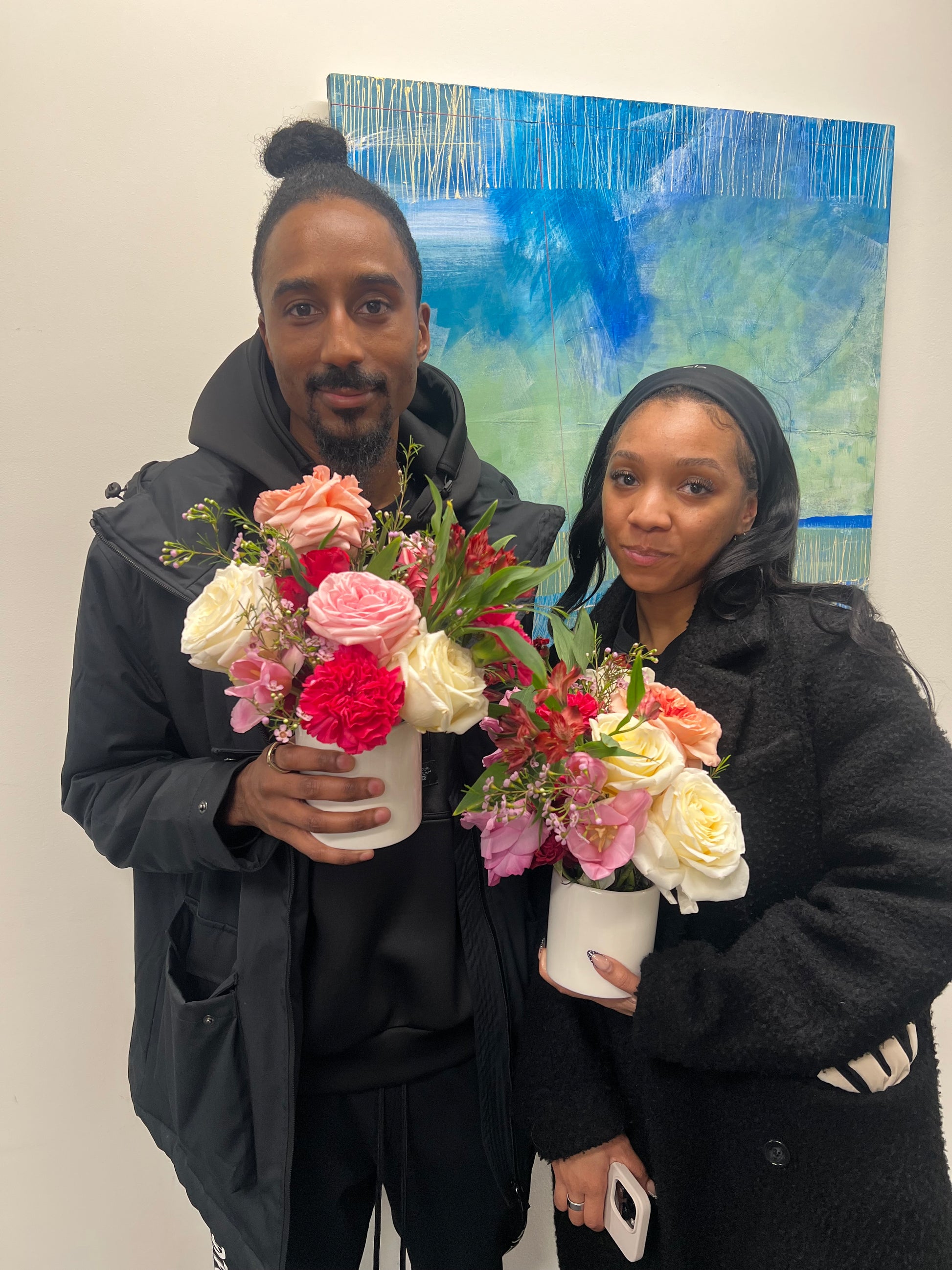 Two people holding flowers with a colorful abstract painting in the background