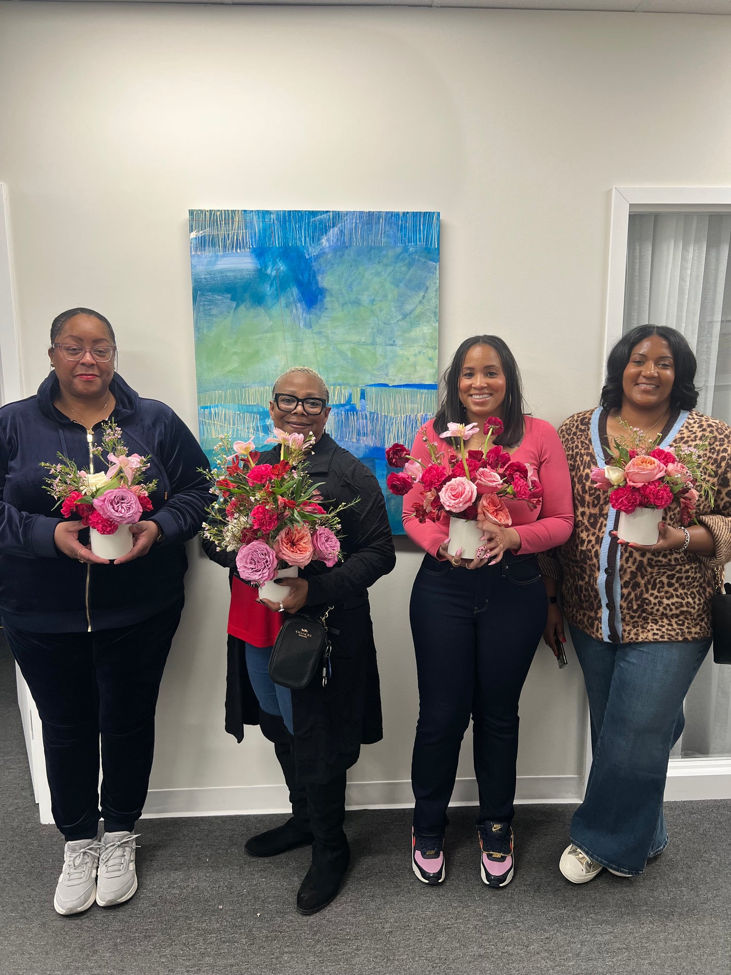 Group of people standing indoors with bouquets of flowers, smiling at the camera.